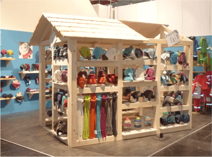 Kleines Holzhaus mit Mützen und Schals bestückt als Ladenbauelement auf Messestand